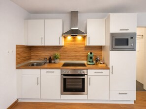 Una cocina moderna con armarios blancos, un horno de acero inoxidable, un microondas y un protector de salpicadero de madera.