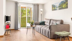 A modern living room with a grey sofa, a small round table, a TV on a stand, and a painting on the wall.