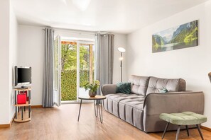 A modern living room with a grey sofa, a small round table, a TV on a stand, and a painting on the wall.