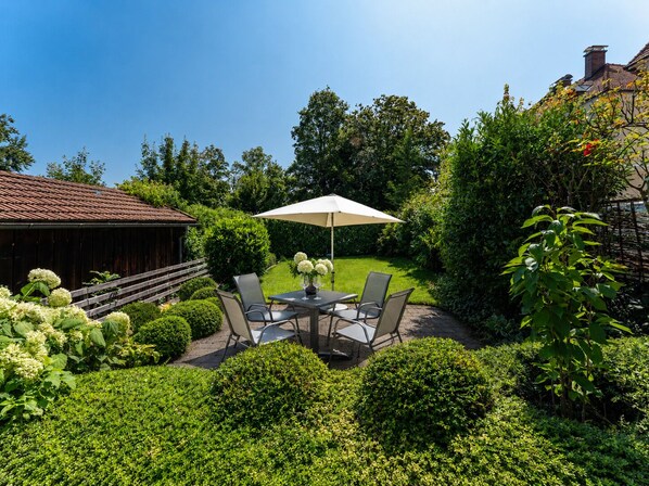 A patio with a table and chairs, surrounded by well-maintained hedges and a wooden fence.