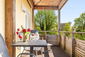 A balcony with a table, chairs, a vase with flowers, and a view of trees and buildings.