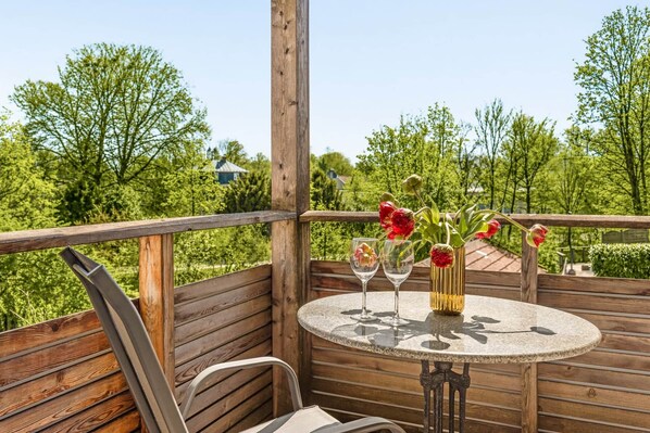 A wooden deck with a round table, two chairs, and a vase with flowers.