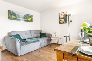A modern living room with a grey sofa, a small round table, and a dining table with a vase of flowers.
