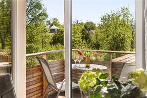 A balcony with wooden railings, a round table with chairs, and a vase with flowers.
