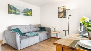 Una sala de estar moderna con un sofá gris, una mesita redonda y una mesa de comedor con un jarrón de flores.