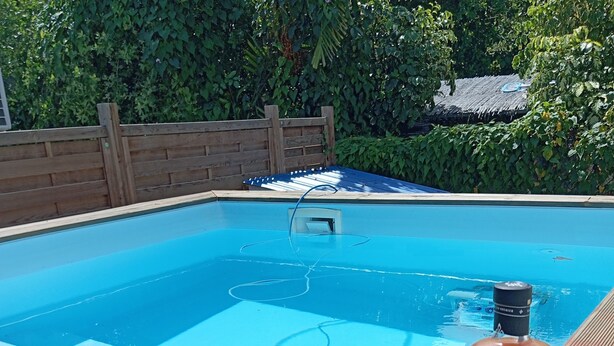 Una terraza de madera con piscina, una botella de licor y un vaso.