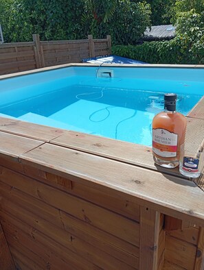Una terraza de madera con piscina, una botella de licor y un vaso.