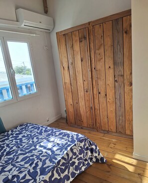 Een slaapkamer met een houten garderobe, een bed met een beddegoed met een patroon, en een airconditioner aan de muur.