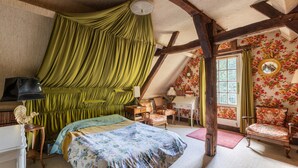 A bedroom with a bed, a desk, a chair, a mirror, and a window with curtains.