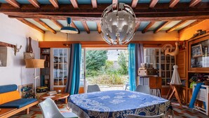 A room with a round table, chairs, a sofa, a bookshelf, and a window with curtains.