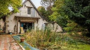 A rustic house with a balcony, a pond, and surrounding greenery.