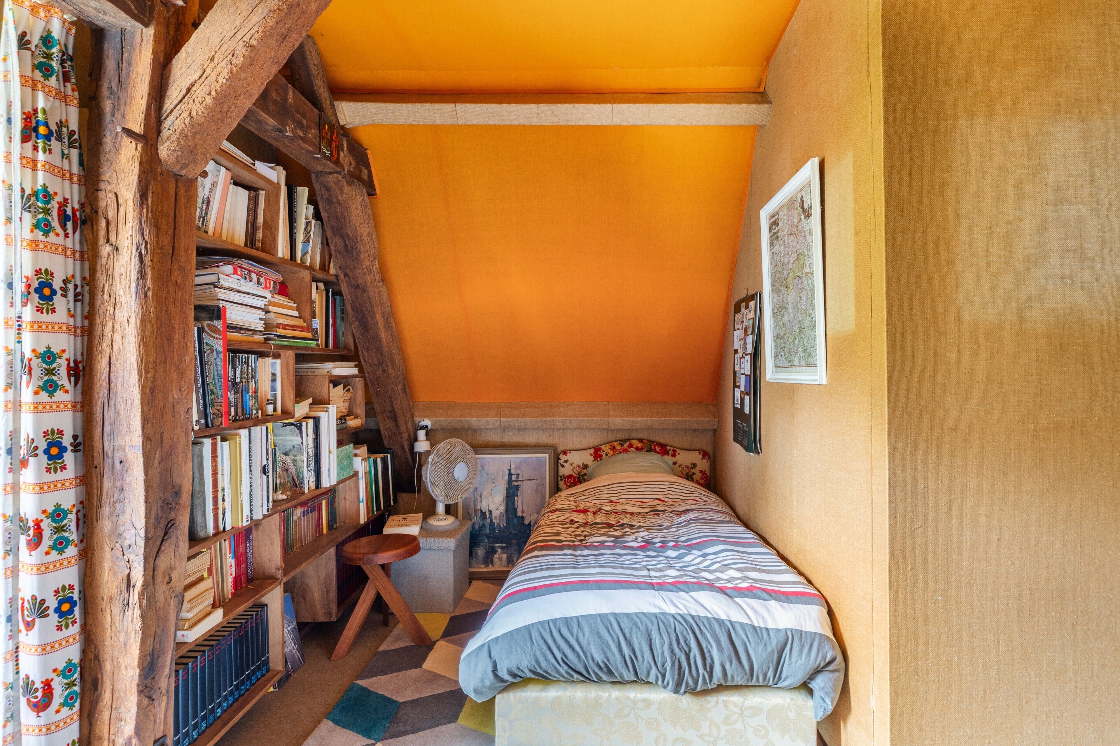 Une chambre confortable avec une bibliothèque en bois, un lit recouvert d’une literie à motifs et une carte accrochée au mur.