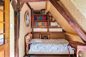 Une chambre avec un escalier en bois, un lit recouvert d’une couvre-lit à motifs floraux, une bibliothèque et un tableau encadré accroché au mur.