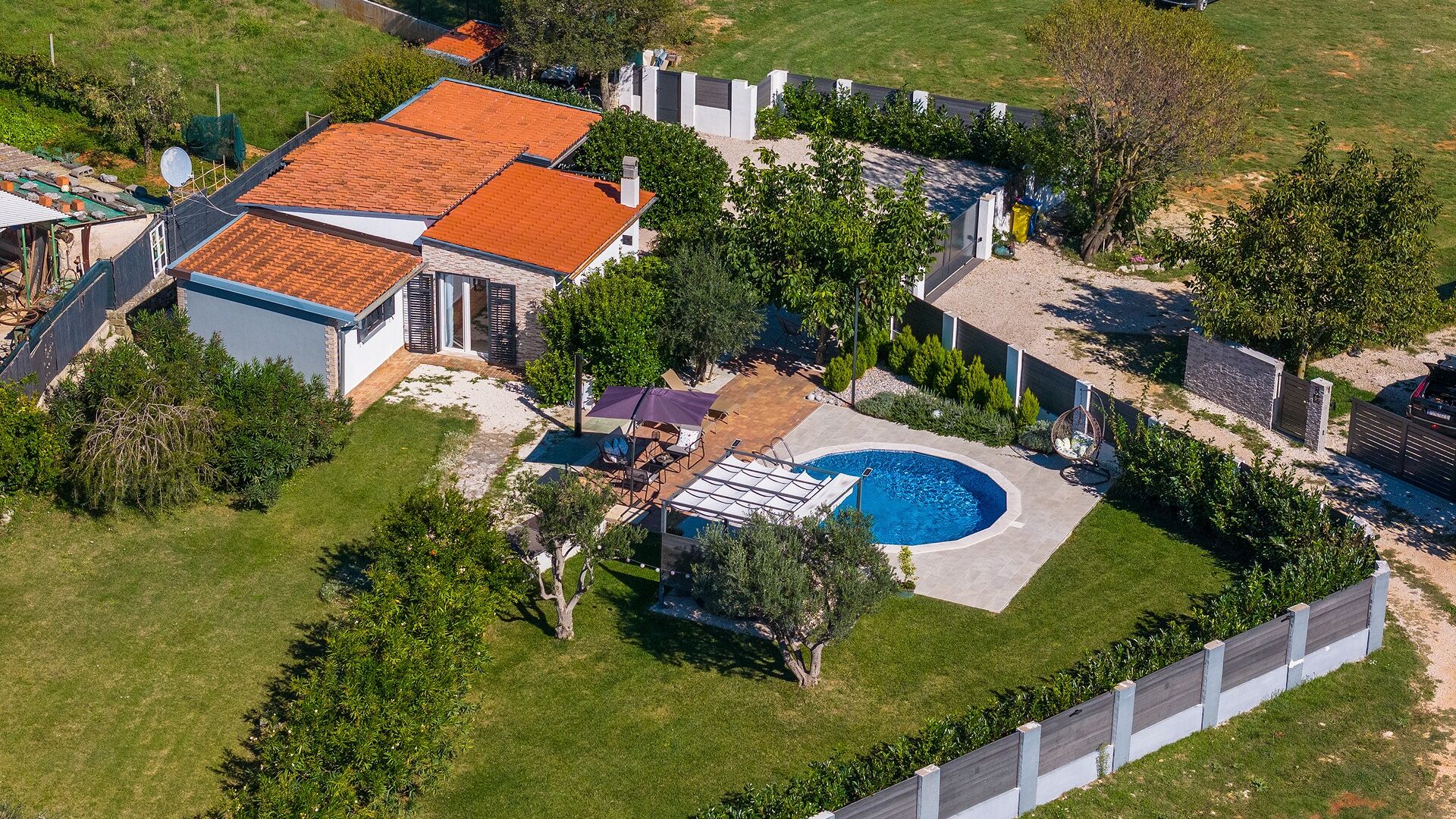An aerial view of a residential property with a swimming pool, a covered patio, and a fenced garden area.