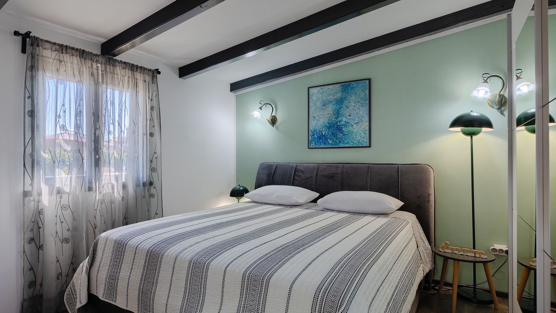 A bedroom with a bed, a painting, a lamp, and a small table.
