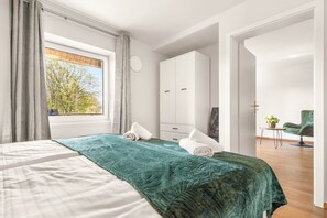 Un dormitorio con cama, armario, escritorio con silla y vistas a árboles por la ventana.