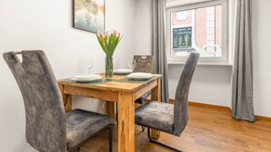 Un comedor con una mesa de madera, cuatro sillas tapizadas de color gris, un florero con flores y una ventana con cortinas.