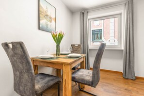 Un comedor con una mesa de madera, cuatro sillas tapizadas de color gris, un florero con flores y una ventana con cortinas.