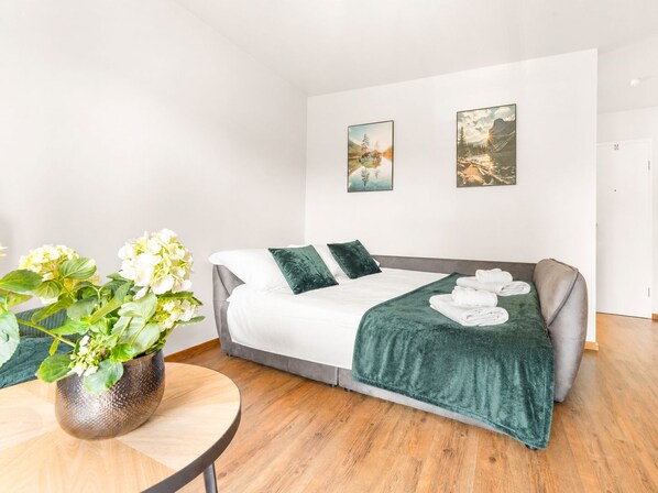 A modern hotel room with a bed, a small table with a plant, and two paintings on the wall.