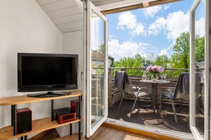 Un balcon équipé d’un téléviseur, de sièges et d’une table agrémentée de fleurs.