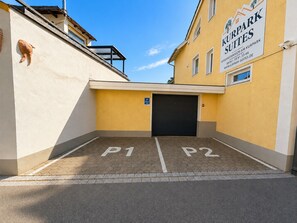 Un espace de stationnement avec deux places délimitées, P1 et P2, et un bâtiment portant une enseigne indiquant « Kurpark Suites ».