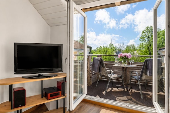 A balcony with a TV, seating, and a table with flowers.