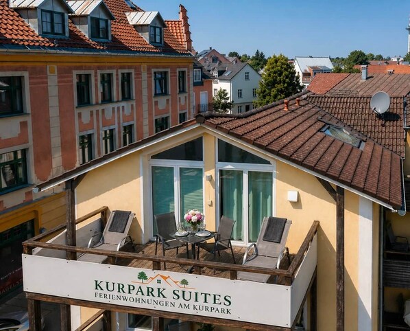 A building with a sign reading 'KURPARK SUITES' and a balcony with chairs and a table.