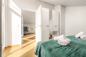 Een moderne hotelkamer met een groene sprei, witte handdoeken, een tafeltje met bloemen en een televisie op de achtergrond.