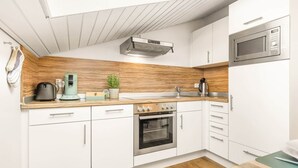 A modern kitchen with white cabinets, a wooden backsplash, a built-in oven, a microwave, and a coffee maker.