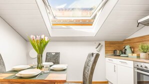 A modern kitchen with a skylight, white cabinets, and a wooden dining table with chairs.