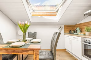 A modern kitchen with a skylight, white cabinets, and a wooden dining table with chairs.