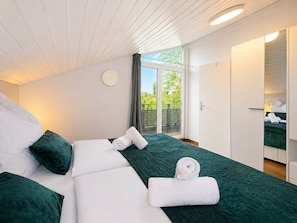 Ein modernes Schlafzimmer mit Bett, grüner Bettwäsche, einem großen Fenster und einer Schiebetür, die auf einen Balkon führt.