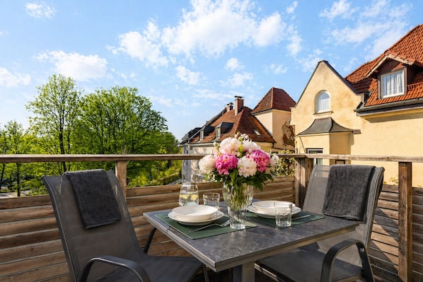 An outdoor dining area with a table set for two, a vase of flowers, and a view of buildings in the background.