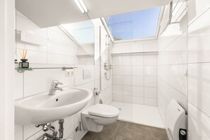 Um banheiro moderno com claraboia, azulejos brancos, pia, vaso sanitário e chuveiro.