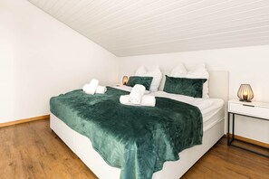 Een net opgemaakt bed met een groene deken en witte kussens, een nachtkastje met een lamp en een houten vloer.