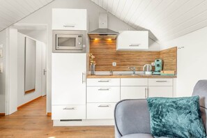 A modern kitchen with white cabinetry, a microwave, a coffee maker, and a wooden backsplash.