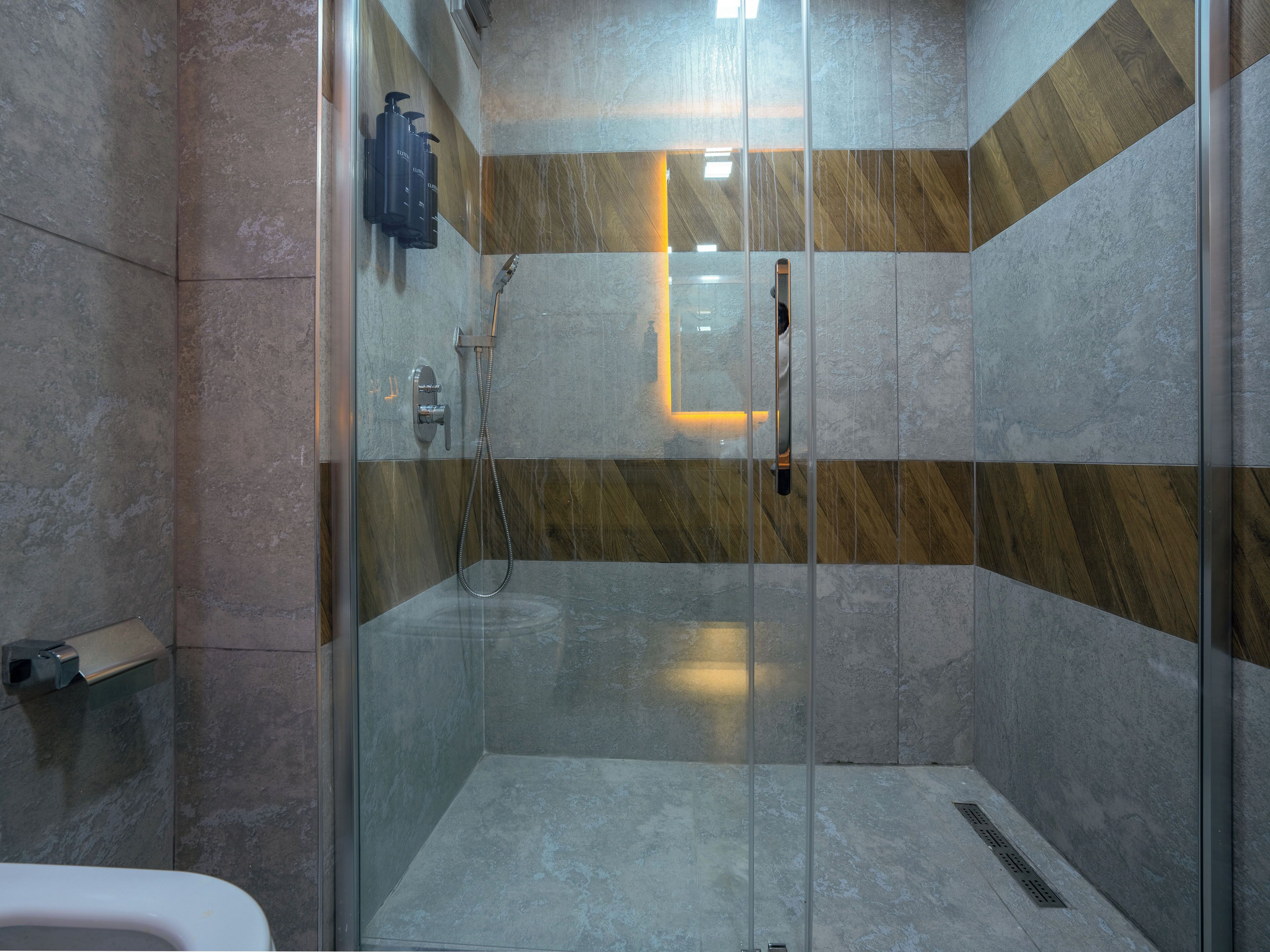 A modern shower area with a glass door, a handheld showerhead, and a wall-mounted faucet.