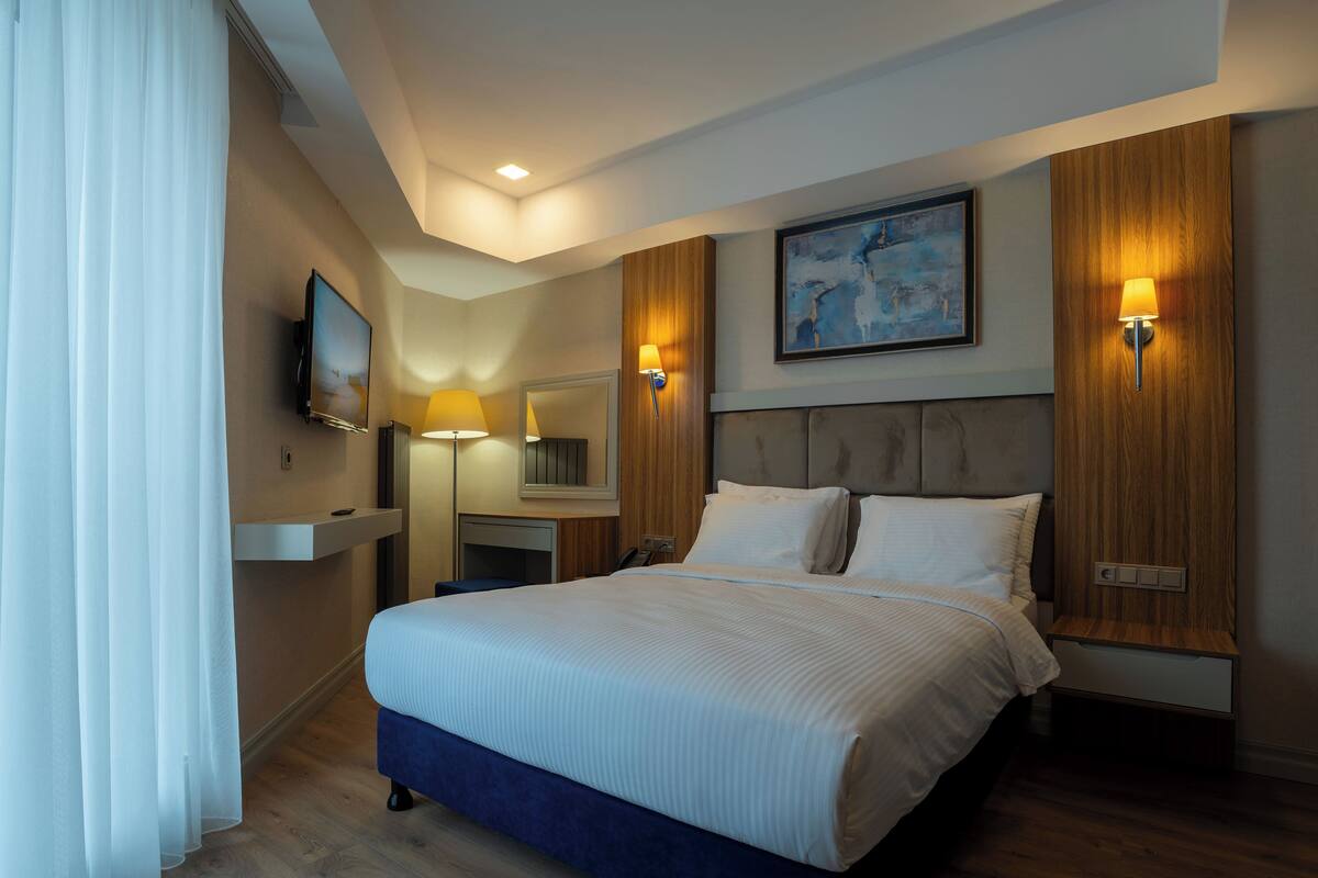 Habitación de hotel con una cama grande, lámparas de noche, un cuadro en la pared y cabecero de madera.