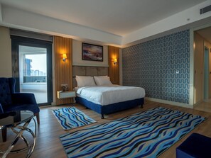 Une chambre d’hôtel moderne avec un grand lit, un coin salon comprenant un fauteuil et une table d’appoint, ainsi qu’un tapis à motifs.