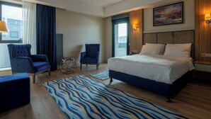 Een hotelkamer met een groot bed, twee fauteuils, een klein bijzettafeltje, een vloerkleed met zebraprint en een schilderij aan de muur.