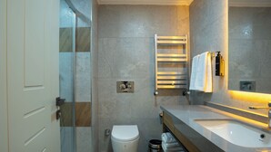 Een moderne badkamer met een douchecabine van glas, een toilet, een wastafel met spiegel en een handdoekhouder.