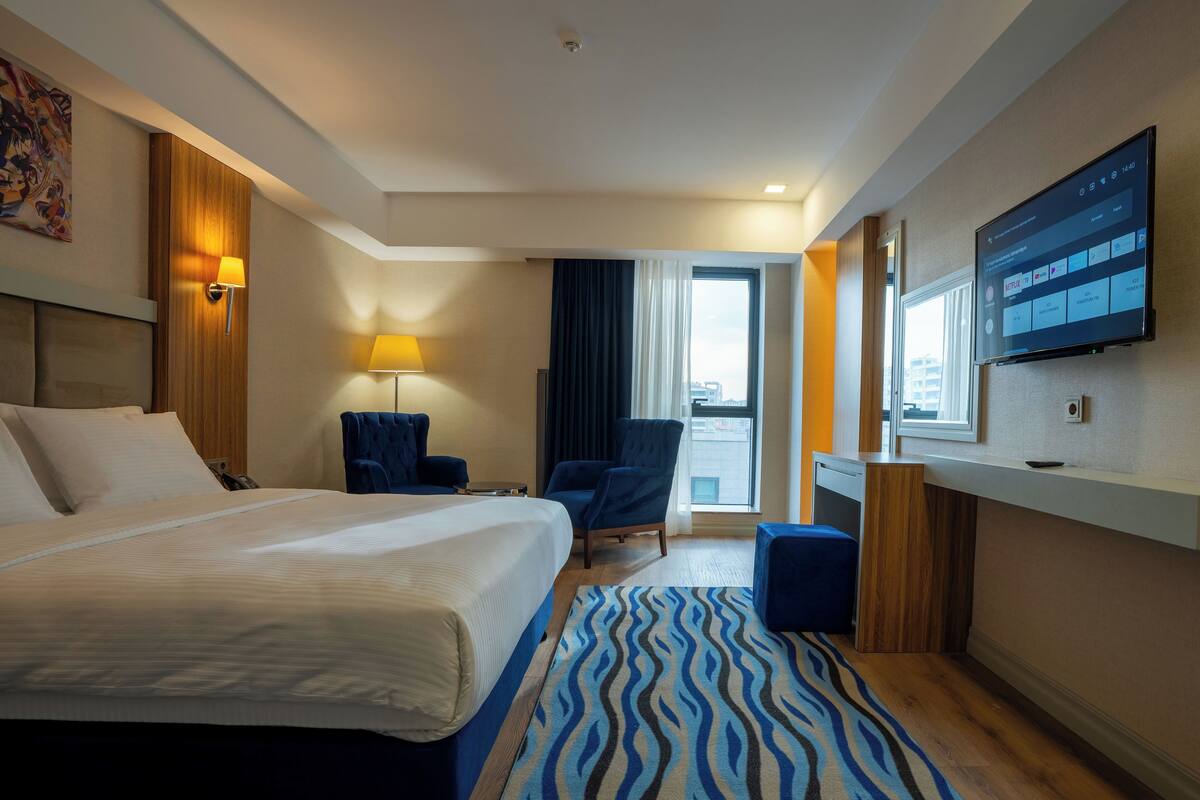 Habitación de hotel con una cama grande, un escritorio, una silla, un televisor y una ventana con cortinas.