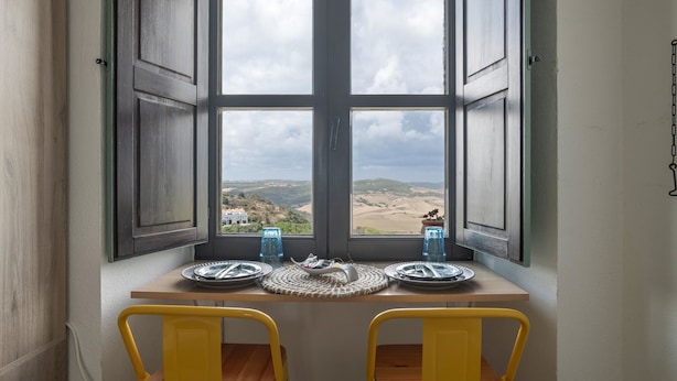 Une table à manger avec deux chaises, une vue par la fenêtre et une porte.
