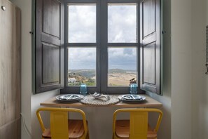 A dining table with two chairs, a view through a window, and a door. - Studio 'Casa Bakara Estudio' with Mountain Views and Wi-Fi (Vejer de la Frontera)