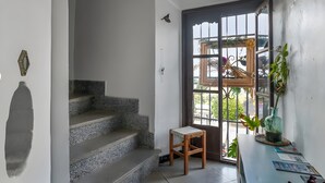 Un escalier menant à une porte donnant sur l’extérieur, un petit tabouret en bois et une plante verte posée sur une table.