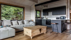 Un intérieur moderne avec un canapé, une table basse en bois, un coin cuisine et de grandes fenêtres.