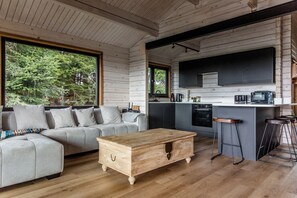 Un interior moderno con sofá, mesa de centro de madera, área de cocina y ventanas amplias.