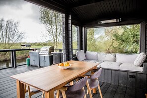 Une terrasse en bois avec une table et des chaises, un barbecue et un canapé avec des coussins.