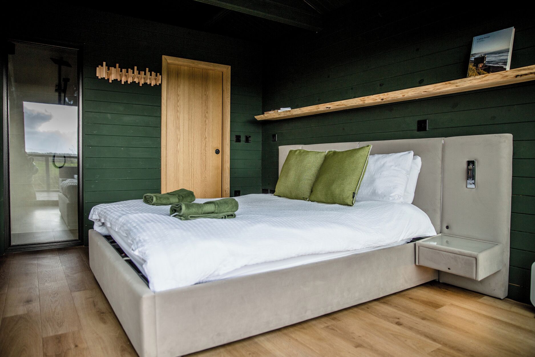 A bedroom with a bed, a wooden door, a shelf, and a nightstand.