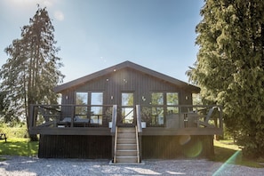 A wooden cabin with a balcony, a staircase, and a view of the surrounding forest.